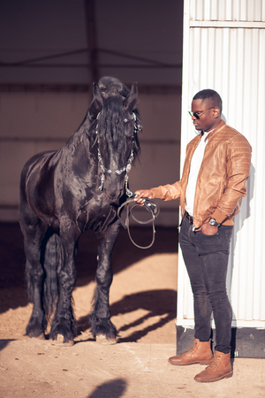 african Man wearing sunglasses near black horse in hangarの写真素材