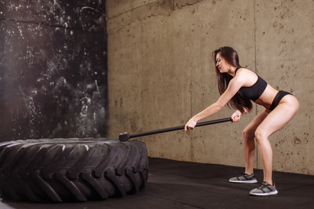 woman smashing large tire with sledgehammer during intense workout in fit gymの写真素材