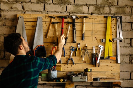 Carpenter man takes hammer from wall with toolsの写真素材