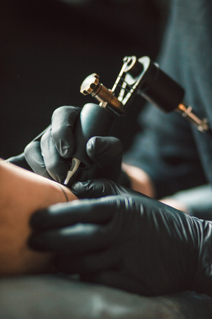 Close up tattoo artist demonstrates the process of getting black tattoo with paint. Master works in black sterile gloves.の写真素材