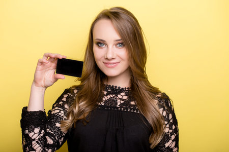 young woman holding bank card isolated on a yellow background