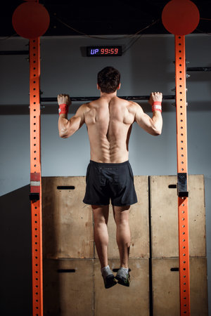 attractive young male adults doing pull ups on bar in cross fit training gym