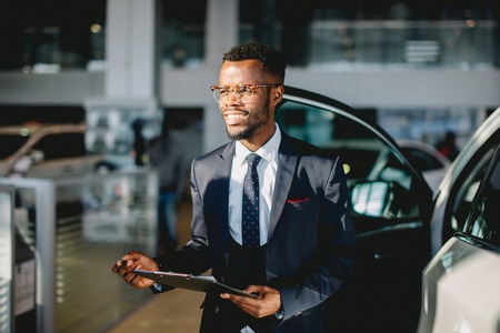 Handsome african car salesman standing at the dealership holding a tabletの写真素材