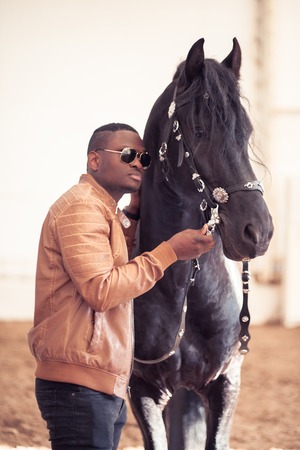 african Man wearing sunglasses near black horse in hangarの写真素材