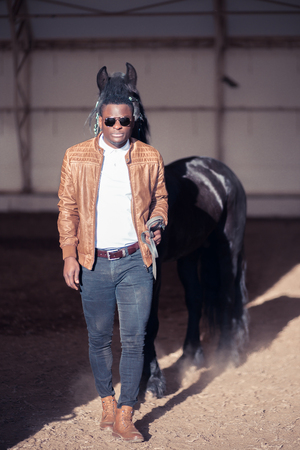 african Man wearing sunglasses near black horse in hangarの写真素材