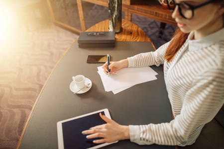 woman writing on paper with digital tablet computer in office roomの写真素材