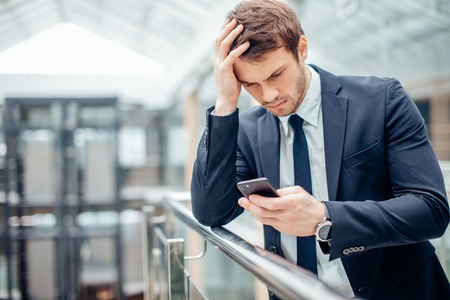 Worried young businessman Read text on mobile phoneの写真素材