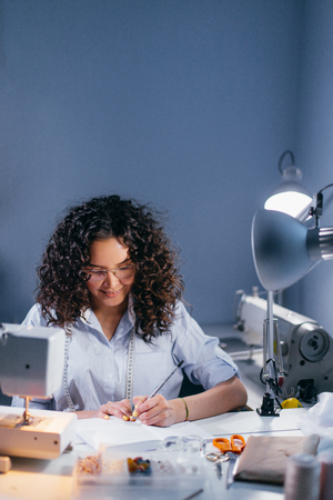 seamstress writing prices of clothers at table in dark room lighted with lampの写真素材