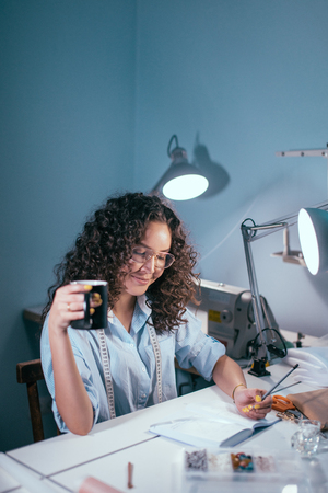 nice dressmaker with mug in hand sitting at the table in the roomの写真素材