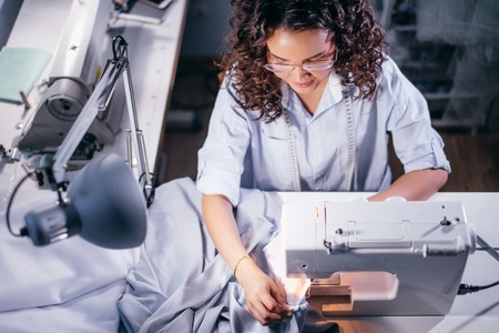 top view photo of seamstress sewing garment on sewing machine in roomの写真素材