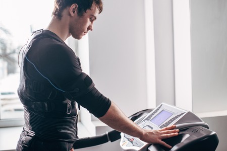 Man in black suit for ems training running on treadmill at gymの写真素材