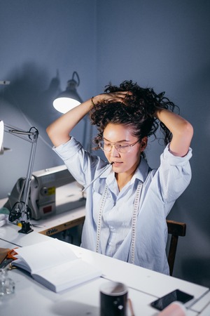 female tailor with pencil in mouth putting her hair back while reading a bookの写真素材