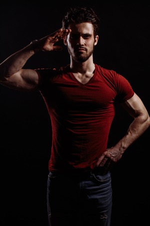 A young handsome man in red T-shirt and jeans is standing in salute poseの写真素材