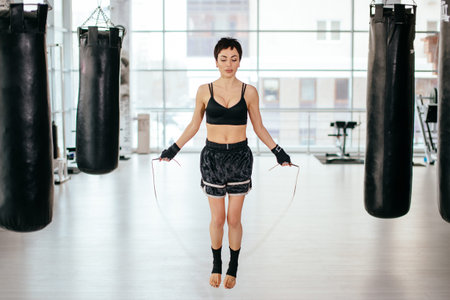 nice female with short black hair is jumping with skipping rope at gym