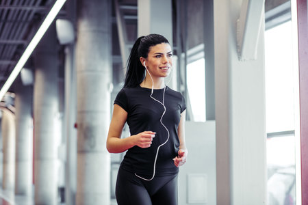 woman with earphones running on indoor track at gym
