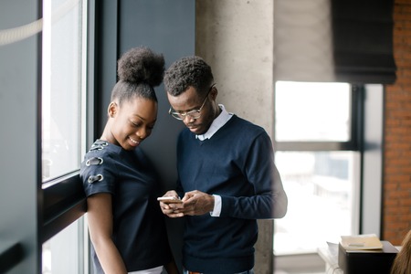 african guy showing something interesting in mobile phone to his black colleagueの写真素材
