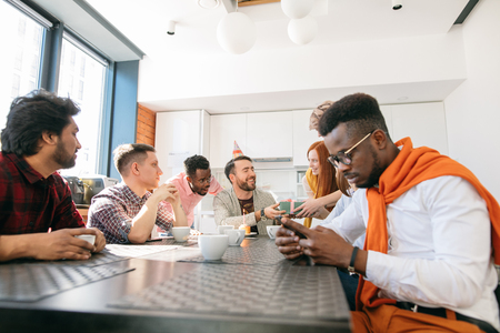 african man is using smartphone while his friends congratulating manの写真素材