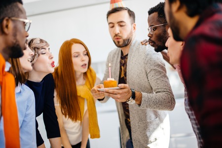attractive man wearing party hat is blowing candle with his friendsの写真素材