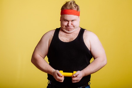 Fat man try to lift small yellow dambbellの写真素材