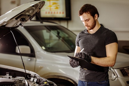 Mechachic checking on car engine and taking notes in clipboardの写真素材