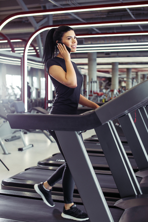 woman smiling while talking on mobile phone while running on treadmillの写真素材