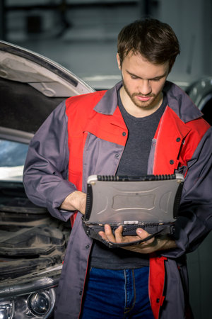 Mechanic Examining Car Engine With Help Of Laptop