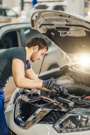 mechanic working under car hood in repair garageの写真素材
