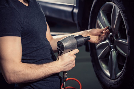 mechanic screwing or unscrewing car wheel by pneumatic wrench