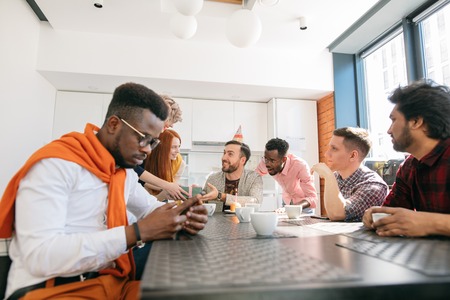 young african guy with mobile phone ignoring his co-workers birthdayの写真素材