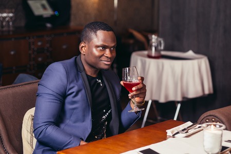 Portrait of handsome afroamerican man in blue jacket drinking wine at restaurantの写真素材