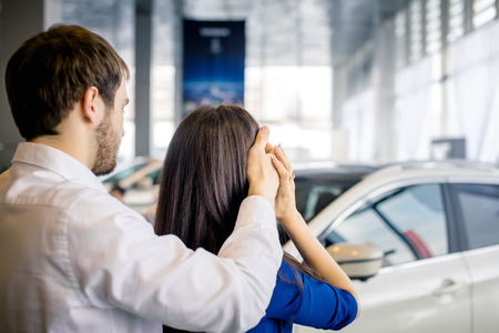Young man is covering the eyes of his girlfriend standing before carの写真素材