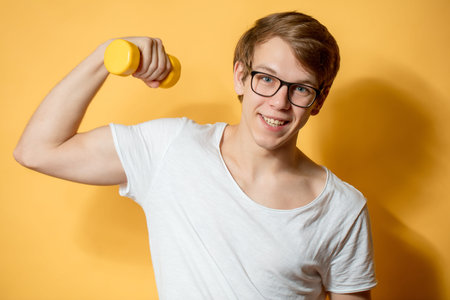 cheerful student doing exercises with yellow dumbbel on the yellow backgroundの写真素材