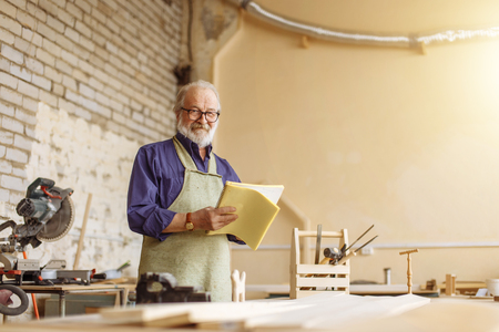 kind grandpa is looking at the camera in the workshopの写真素材