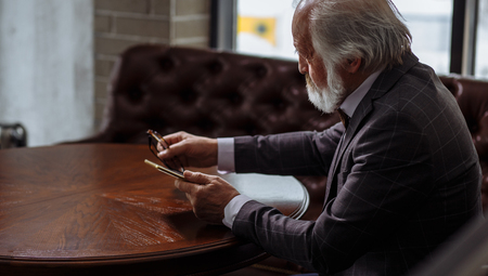 photo of old man holding glasses and smartphone on the handsの写真素材