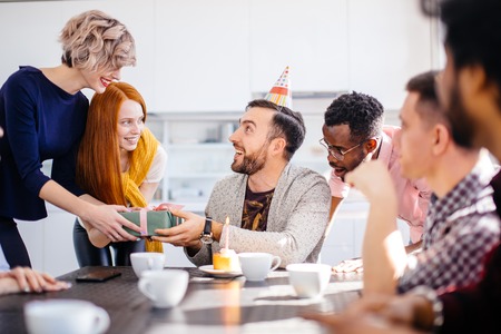 young bearded man wearing bithday cap getting pleasant giftの写真素材