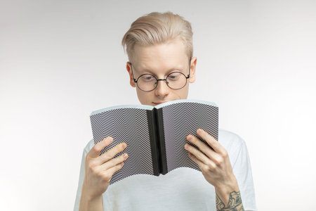 White man smile and hides his face behind a book. Studio portrait