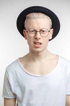 Annoyed blond male in black hat with frowned face as recieving unpleasant newsの写真素材