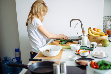 Portrait of happy female wife in white t-shirt cooking dinner at kitchenの写真素材