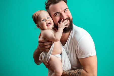 Playful father carrying his smiling infant child on neck over blue background