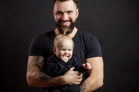 Young athletic father with adorable baby on black background