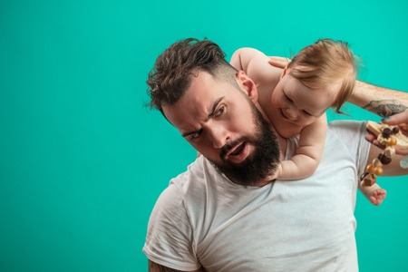 Playful father carrying his smiling infant child on neck over blue backgroundの写真素材