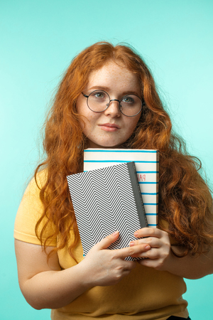 Redhead young woman holding blank books looking at the camera isolated on blueの写真素材