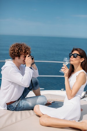 Attractive couple on the yacht. Young man is taking photo of his girlfriendの写真素材