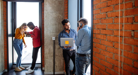Confident young businessman using smartphone standing at the window in office