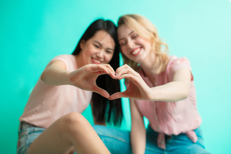 Young girls showing heart sign with their hands sitting over blue backgroundの写真素材