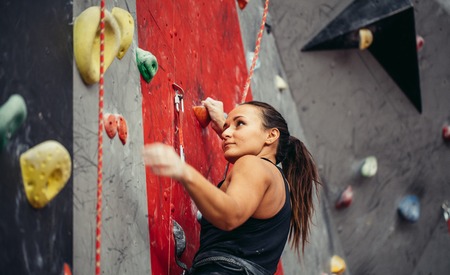 Beautiful young strong woman climbing on red artificial wall top view.の写真素材