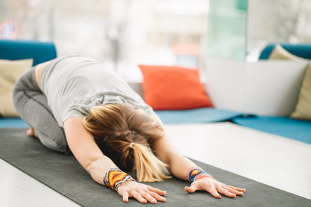 Fitness female performing yoga Child Pose on exercise mat at gym.