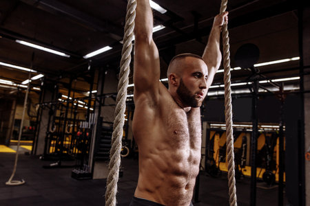 close up side view photo. bearded handsome athlete with raised arms and rope