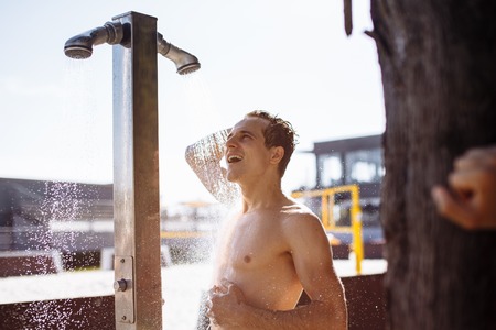 Handsome young topless caucasian man taking an outdoor shower on beach.の写真素材