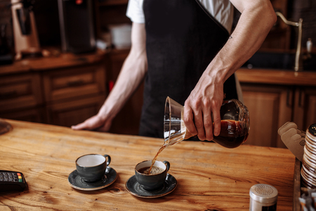 waiter is pouring ground coffee in the cups for visitorsの写真素材
